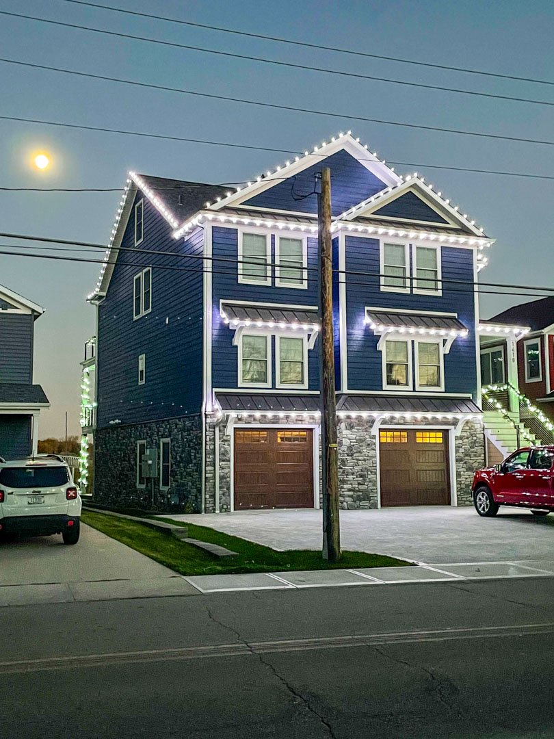 White Christmas lights outlining a blue home at dusk
