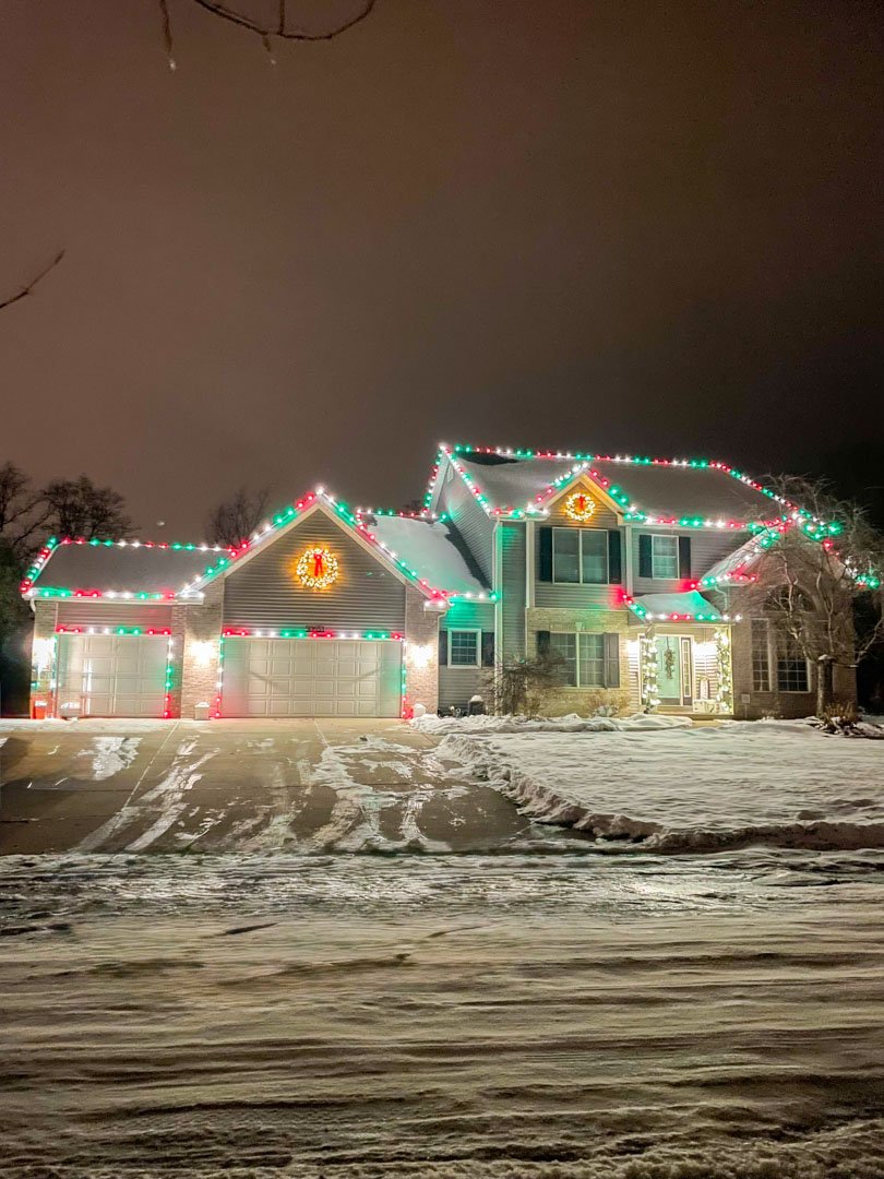 Red and green roofline lighting on a snowy home at night